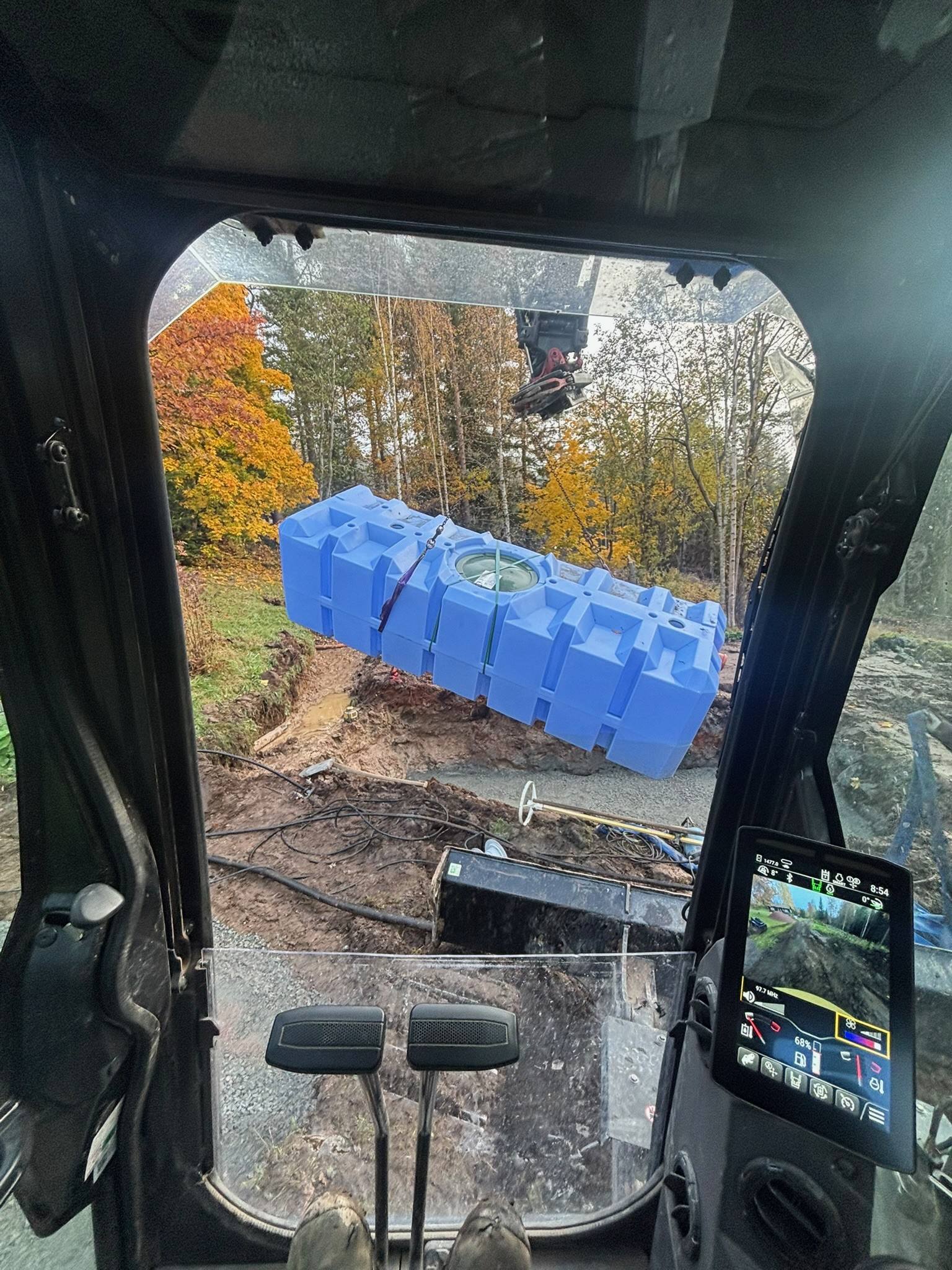 Sluten tank som lyfts på plats med grävmaskin, sett från hytten
