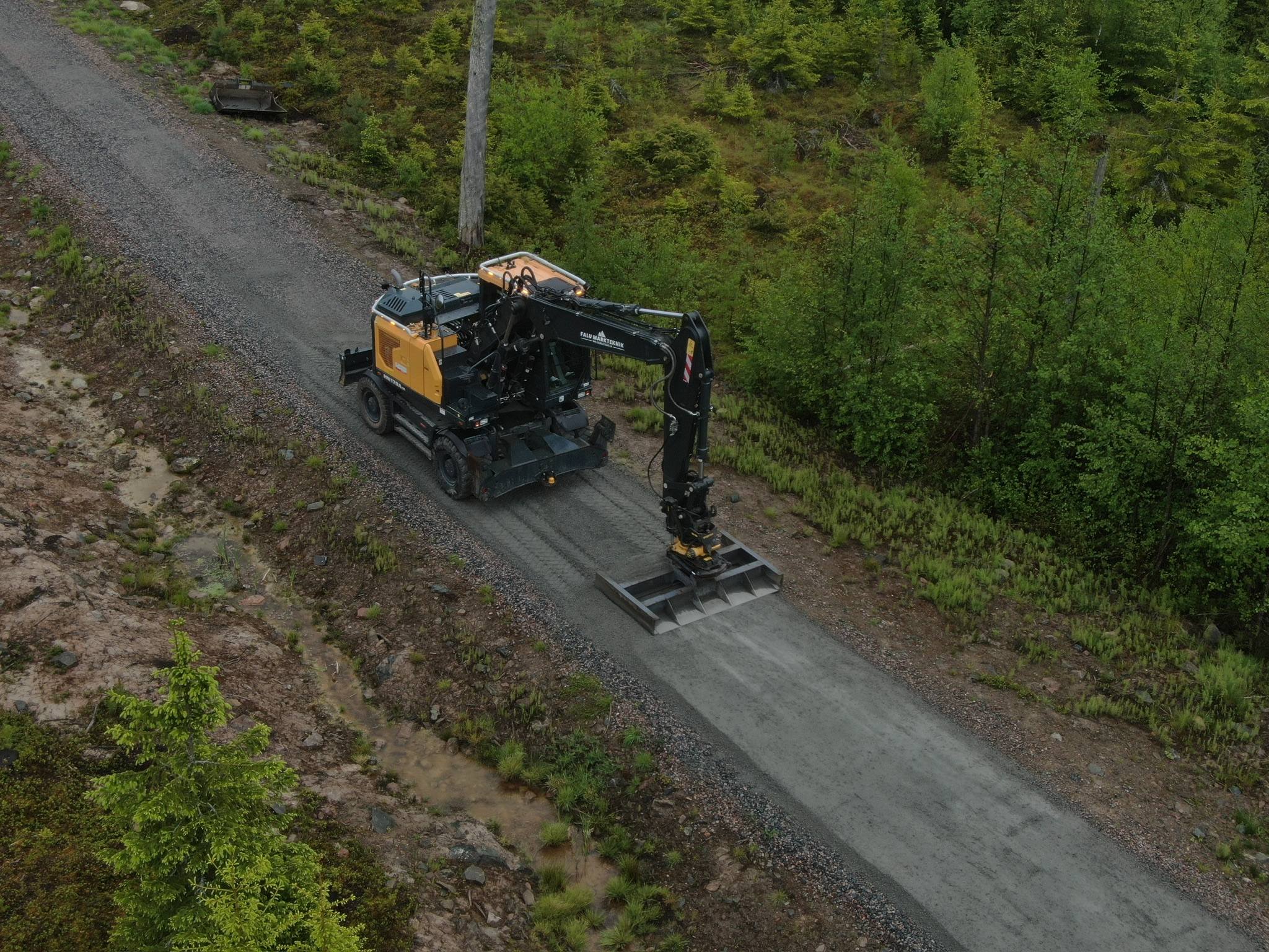 Grävmaskin som drar av en grusväg i skogen