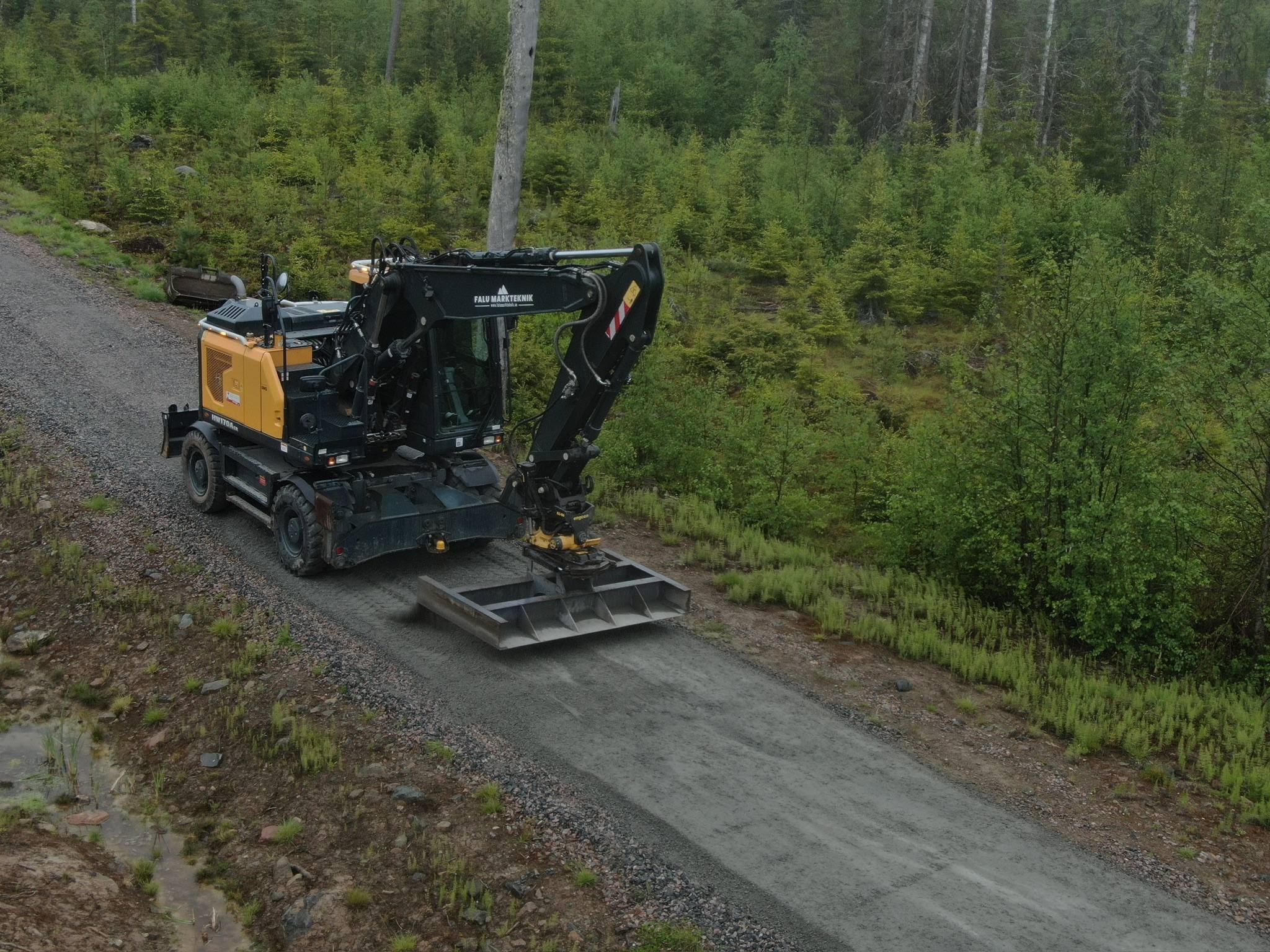 Grävmaskin med väghyvelblad på en skogsbilväg