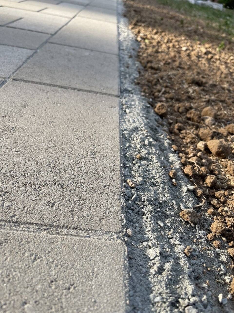 Lagda betongplattor med skuren kant mot sättsand och jord